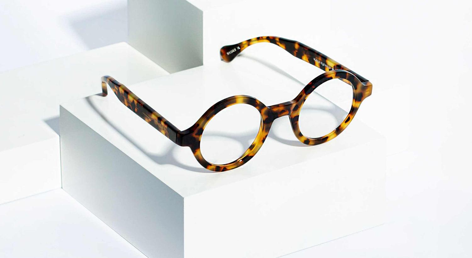 Angled view of round eyeglasses placed on white 3D platform.