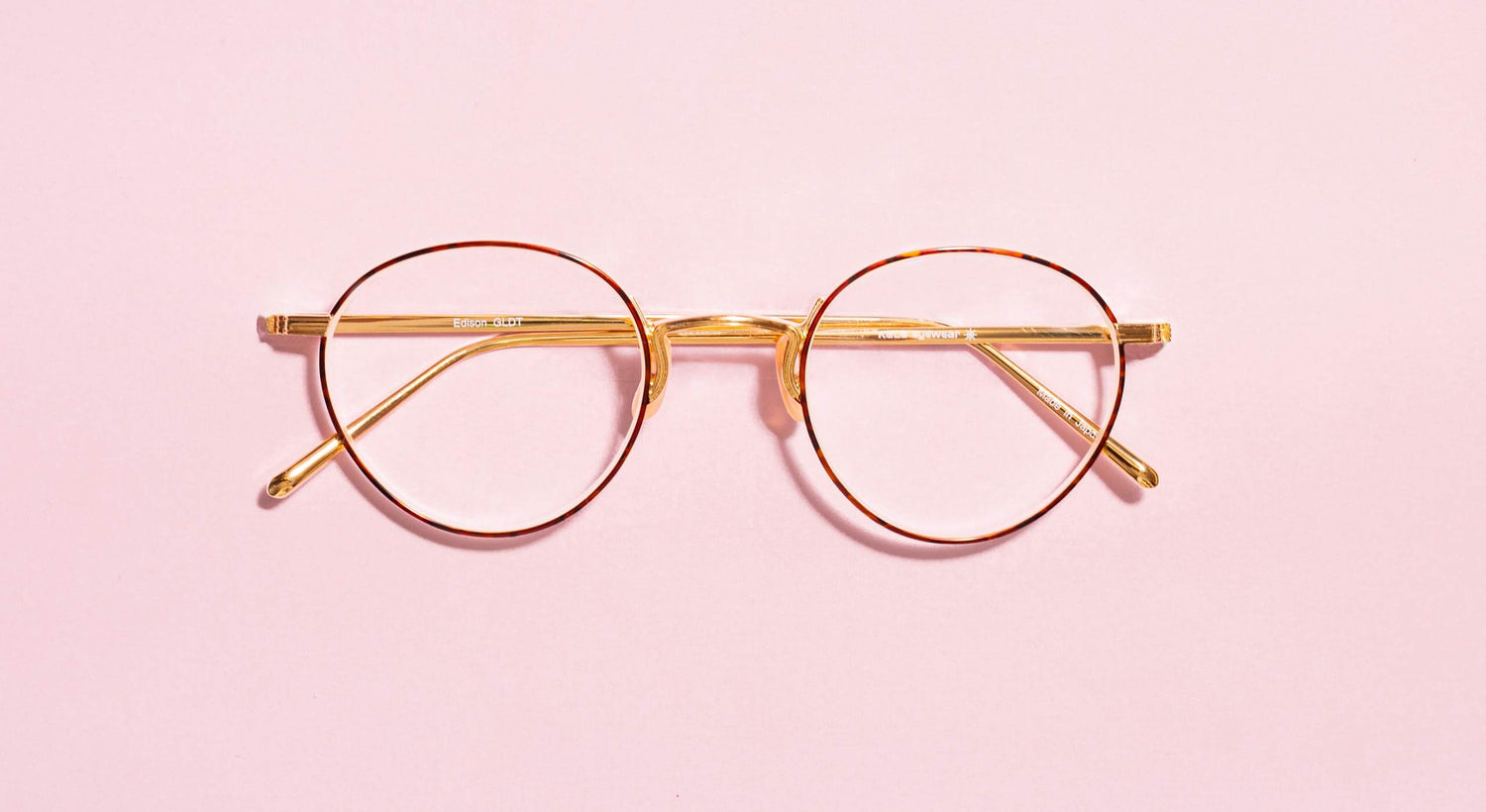 Pair of round eyeglasses with temples folded in sitting on a flat surface.