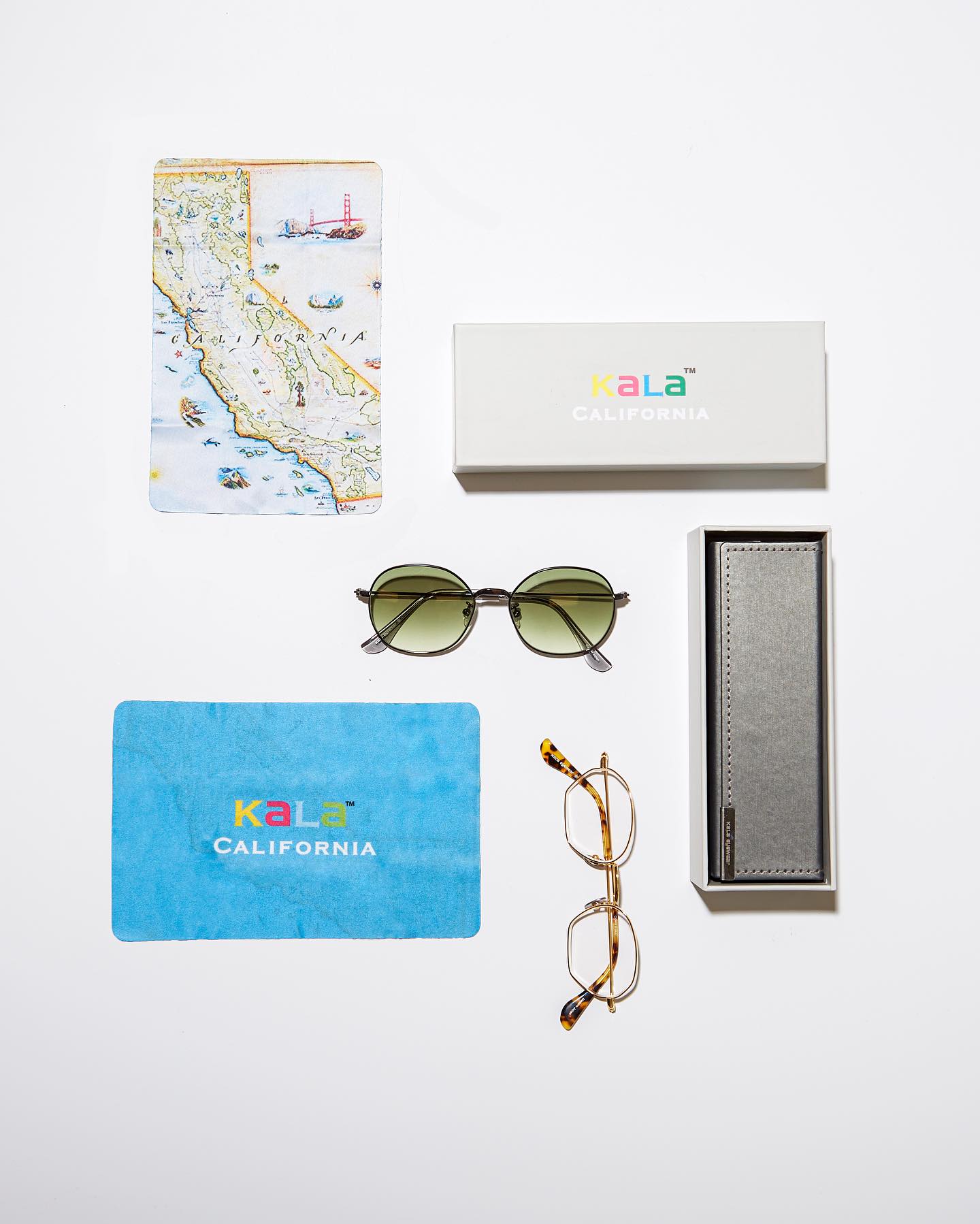 Looking down on neatly arranged objects - a map of California, a pair of sunglasses with green lenses, a pair of eyeglass frames, a microfiber cleaning cloth, a branded box and a case for the frames.